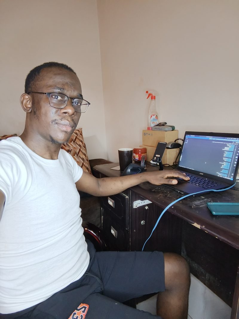 Brian, wearing glasses, seated at a wooden desk with a Dell laptop showing code, May 2025