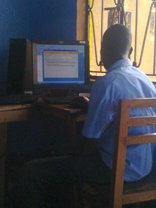 Brian seated at a desktop computer with a monitor and PC tower in a simple room with a blue wall, photographed in November 2014