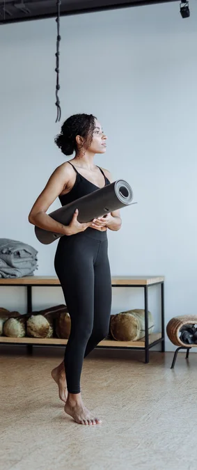 Black woman holding a yoga mat in a studio