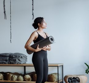 Black woman holding a yoga mat in a studio