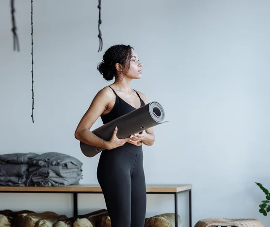 Black woman holding a yoga mat in a studio