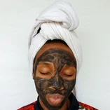Black woman applying a clay skincare mask