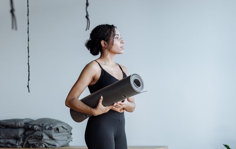 Black woman holding a yoga mat in a studio