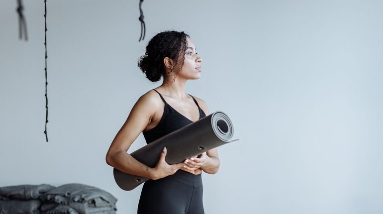 Black woman holding a yoga mat in a studio
